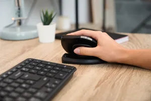Main utilisant la souris ergonomique Contour Unimouse en position verticale sur un bureau, à côté d'un clavier